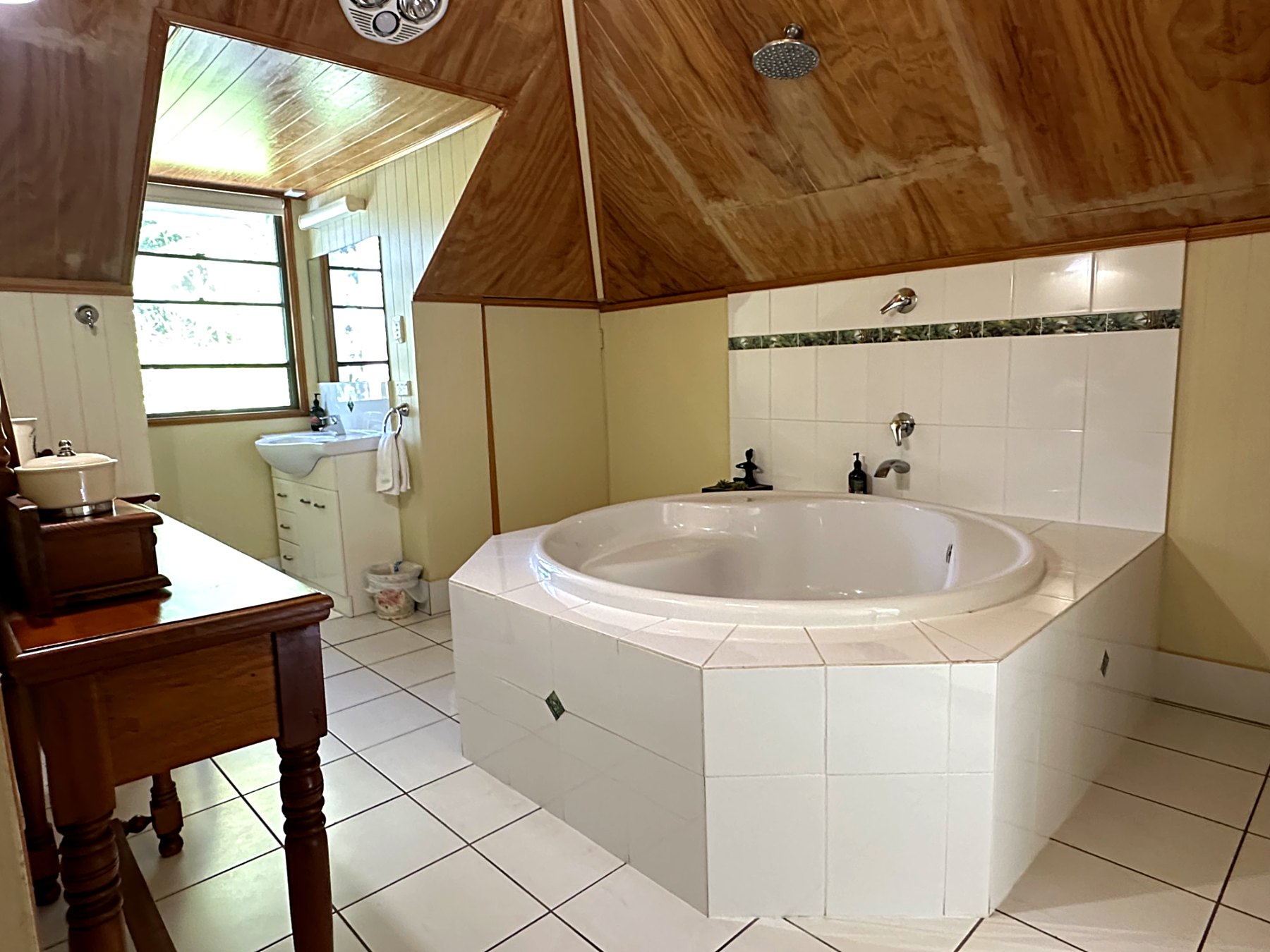 A round spa bath set into tiles, under the same cathedral timber ceiling, with a rain shower