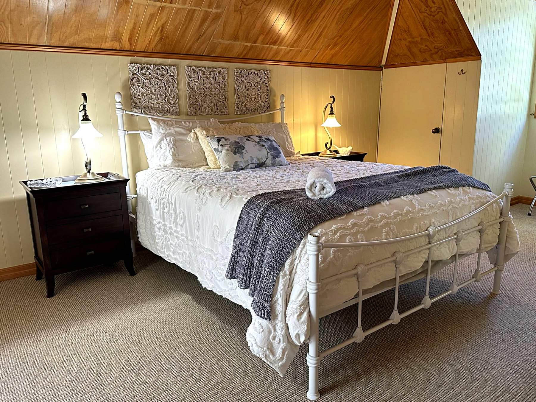 A bedroom with a white iron bed frame and cathedral timber ceiling