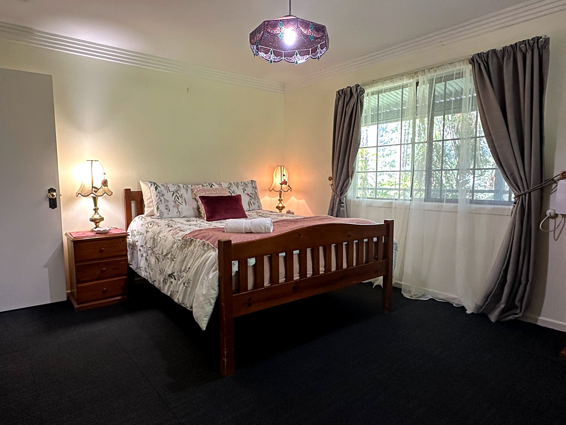 A cosy bedroom with a queen bed, floral bedding and warm bedside lamps